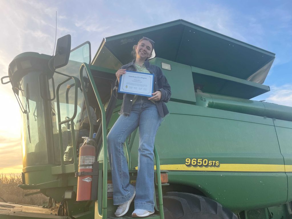 daughter, Linda LeDuc, standing on farm machine, holding her American FFA degree